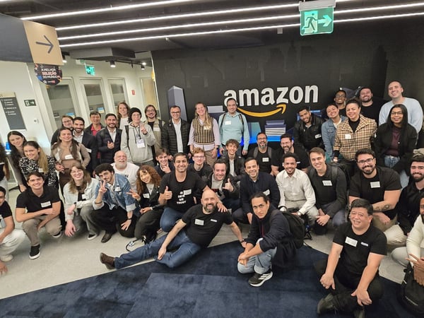 A large group of people posing for a team photo inside an Amazon office building, with a prominent Amazon logo on the wall behind them.