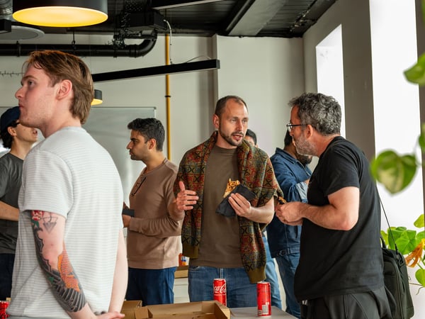 A group of men are socializing and eating pizza during a casual indoor gathering or office break.