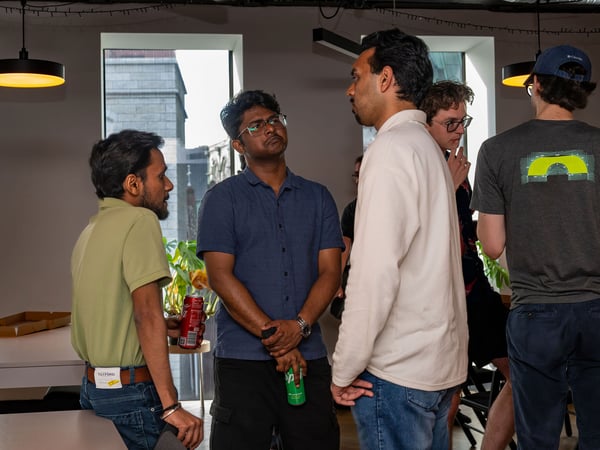 A group of young men are standing and chatting in a modern office or event space during a casual social gathering.