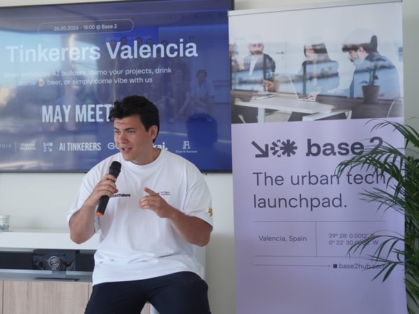 A man speaks into a microphone during a tech meetup presentation in front of a screen and banner.
