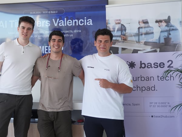 Three young men posing together indoors in front of a presentation screen and promotional banner.