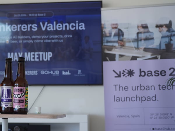 Three craft beer bottles stand on a table in front of a presentation screen displaying 'AI Tinkerers Valencia' and a banner for 'base 2'.