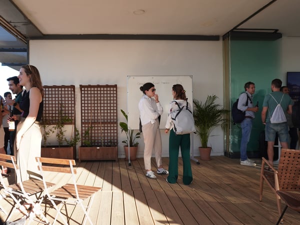A group of people socializing and talking on an outdoor wooden terrace with a whiteboard in the background.