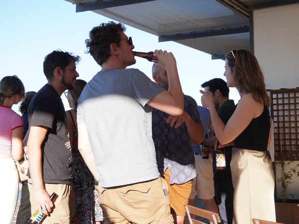 A group of people socializing and enjoying drinks on an outdoor balcony during a sunny day.
