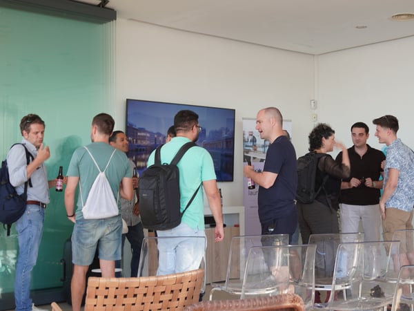 A group of people standing and socializing in a modern indoor event space with transparent chairs in the foreground.