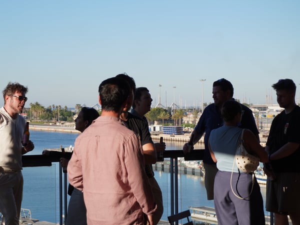 A group of people socializing outdoors on a balcony overlooking a harbor.
