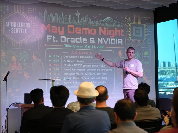 A presenter stands on stage in front of a projected slide showing the agenda for an 'AI Tinkerers - Seattle' event, with an audience seated in the foreground.