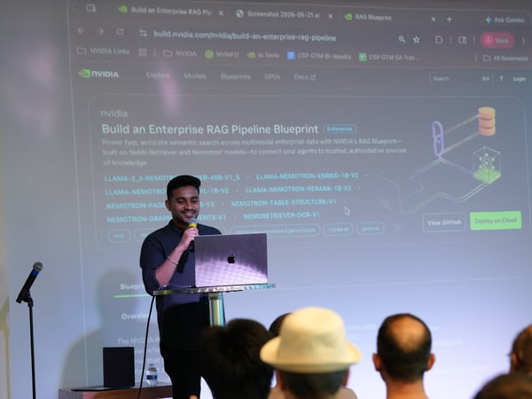A man stands at a podium presenting a slideshow on a large projector screen displaying an NVIDIA website about building an enterprise RAG pipeline, while an audience watches from the foreground.