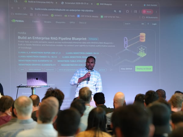 A man stands on a stage speaking into a microphone during a presentation, with a large screen behind him displaying an NVIDIA webpage about building an enterprise RAG pipeline.
