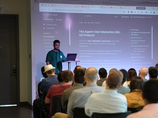 A man stands on a stage presenting 'The Agent-User Interaction (AG-UI) Protocol' to an audience, with the documentation projected on a large screen behind him.