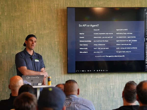 A man stands next to a large display screen presenting a slide titled 'So API or Agent?' to an audience.