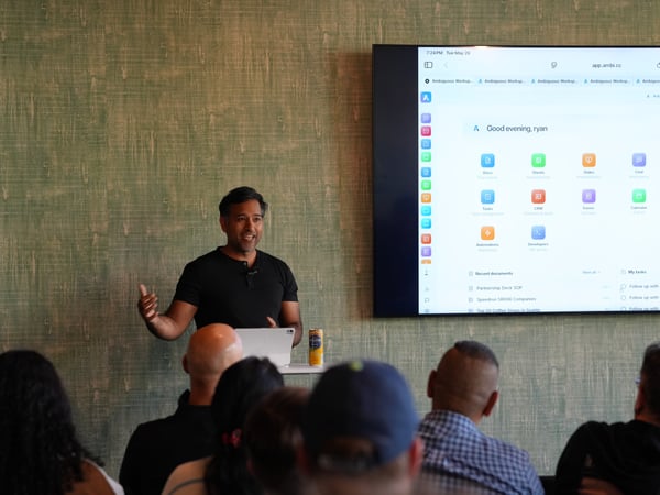 A man stands presenting in front of a large screen displaying a software interface to an audience.