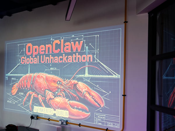 A photograph showing a digital graphic projected onto a white wall, featuring the text 'OpenClaw Global Unhackathon' and a detailed illustration of a robotic lobster.