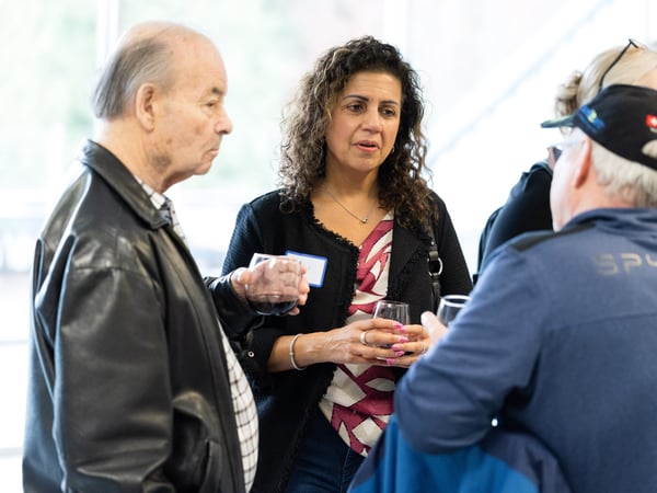 A group of people are engaged in conversation at a social gathering, holding drinks and wearing name tags.