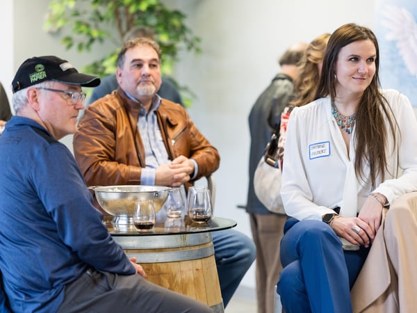 A candid photograph of people attending a social gathering indoors, featuring a woman in a white blouse and a name tag in the foreground.