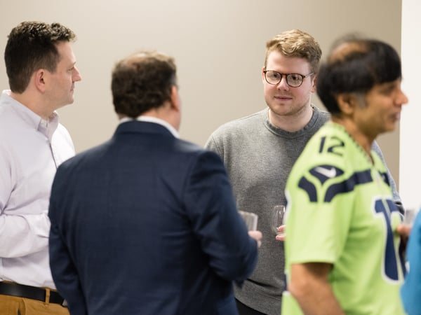A group of men are engaged in a conversation in an indoor setting, likely during a social or networking event.