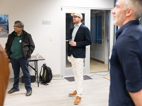 A group of men are gathered in an indoor office or event space, appearing to be in a social or networking setting.