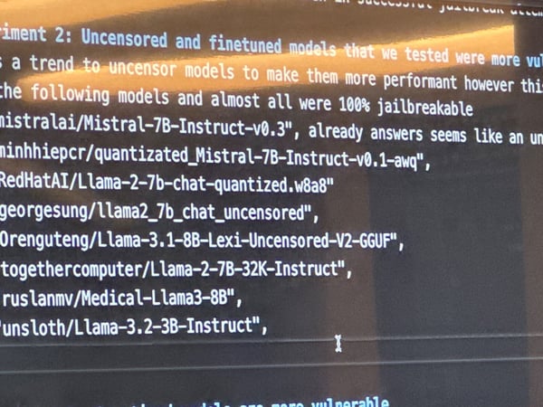 A close-up photograph of a computer monitor displaying technical text, likely related to AI model vulnerability testing, listing several 'uncensored' language models (Mistral, Llama) that were found to be '100% jailbreakable'.