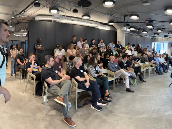 A wide-angle photograph capturing a large audience seated in a modern, industrial-style room attending a presentation or meeting.