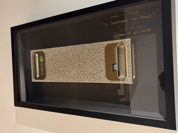 A photograph of a framed NVIDIA GPU mounted on a wall, featuring a handwritten message and signature on the glass addressed to Aidan N. Gomez.