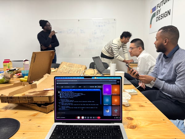 A group of people collaborating in a modern workspace, with a laptop in the foreground showing a code execution plan and others working at a whiteboard in the background.