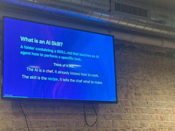 A photograph of a television screen mounted on a brick wall, displaying a presentation slide about AI skills.