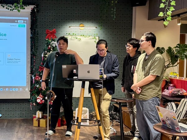 A photograph captures four men gathered around a laptop and a projected screen displaying a website interface for a product called "LinkHub" during an indoor presentation or demo, with Christmas decorations visible nearby.