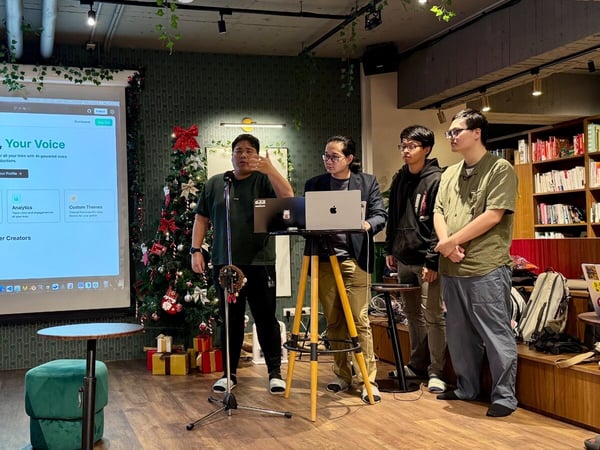 A photograph capturing four men during a product presentation indoors, where one speaker is gesturing near a microphone stand while a website interface (LinkHub) is projected onto a large screen.