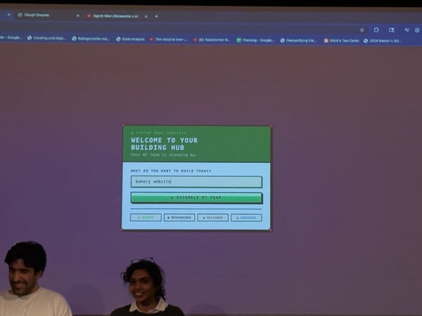 A photo of two people smiling in front of a large screen displaying a web application interface for an AI-powered building hub.