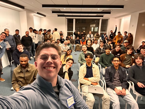 A large group of people, primarily young adults, posing for a selfie in a modern indoor office or event space.