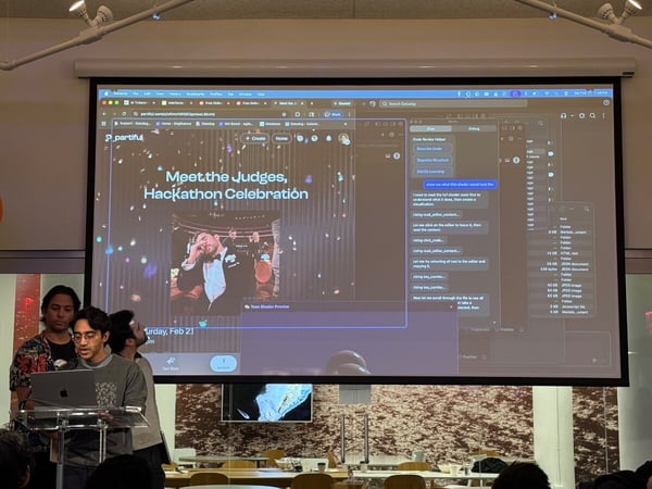 A group of young men are giving a presentation at a podium in front of a large screen displaying a 'Meet the Judges, Hackathon Celebration' event page and a coding assistant interface.