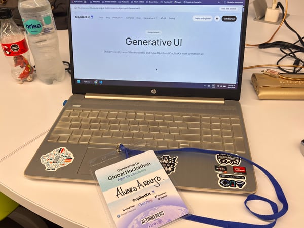 A laptop on a white desk displays a website for CopilotKit, with a hackathon name tag for Alvaro Araujo resting on the keyboard.