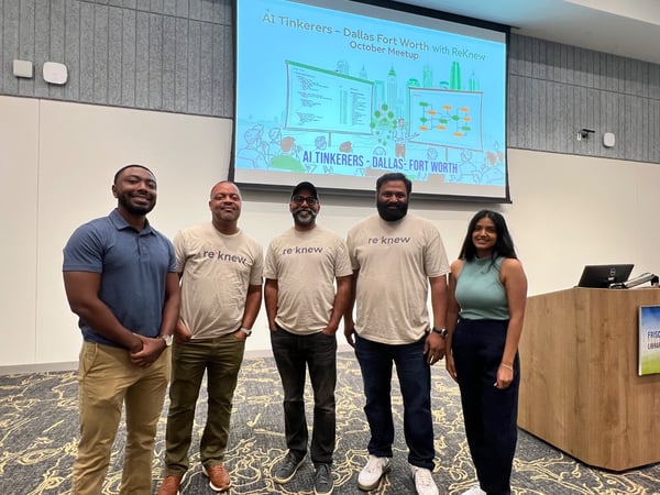 Five individuals, four of whom are wearing matching 're knew' branded shirts, pose for a group photo in front of a presentation screen detailing an 'AI Tinkerers - Dallas Fort Worth' meetup. The setting appears to be an indoor event space or library meeting room.