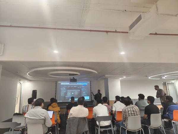 A wide-angle photograph captures an indoor professional presentation or training session where a large audience is seated, facing a presenter who is demonstrating software on a large projection screen.