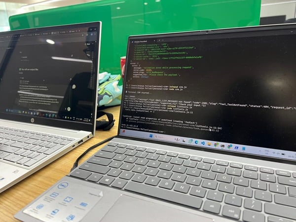 The image shows two laptops sitting on a desk, with the foreground laptop displaying a terminal window filled with code error messages and debugging logs.