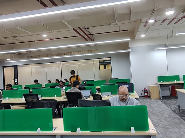 A wide-angle shot of a modern indoor office space where several people are working at desks separated by bright green dividers.