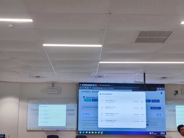 A photograph showing a large indoor room with digital screens displaying a schedule for an 'AI Tinkerers' hackathon event in Monterrey.