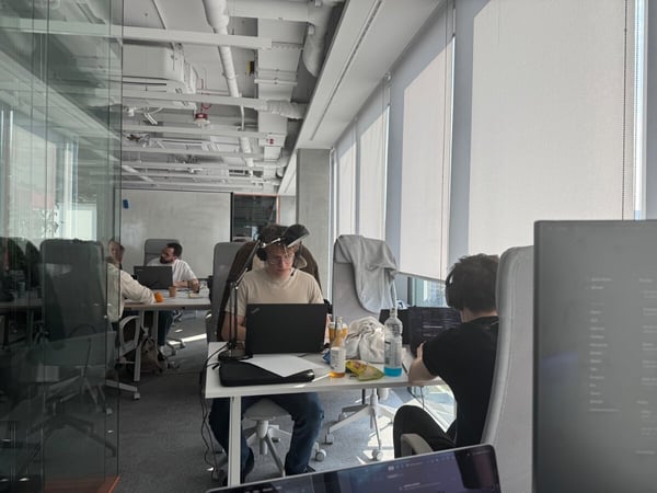 A modern, open-plan office space where several people are focused on their laptops at white desks.