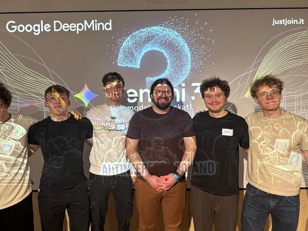A group of five young men posing for a photo in front of a projection screen at a Google DeepMind hackathon event.