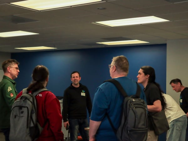 A group of people are gathered in an indoor space, likely an office or event venue, engaged in a conversation.