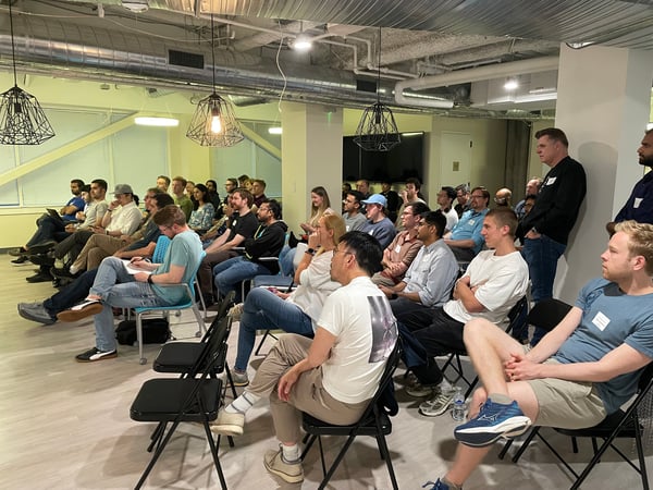 A candid photograph capturing a large audience seated in rows, attentively watching an unseen speaker during an indoor professional event or presentation.