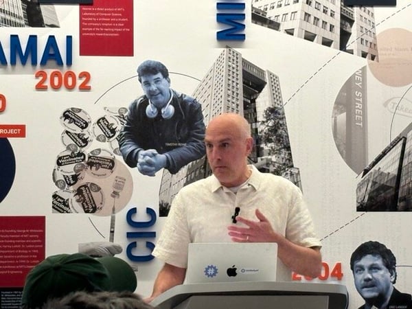 A man stands at a podium giving a presentation in front of a wall mural detailing historical milestones.