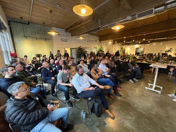 A large group of people are seated in an industrial-style office space, attending a presentation or event.