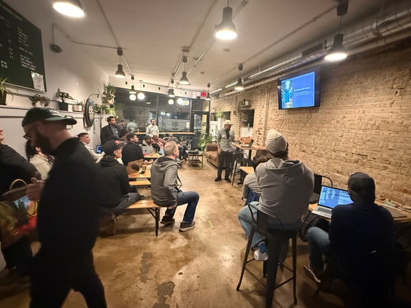 A group of people are gathered in a room with an exposed brick wall, watching a presentation titled 'The Problem With Bridging' on a wall-mounted screen.
