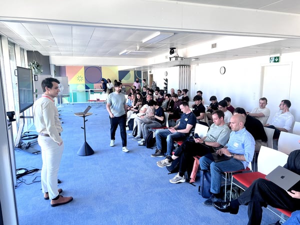 A group of people attending a presentation or event in a modern office space with blue carpeting and a colorful geometric mural.