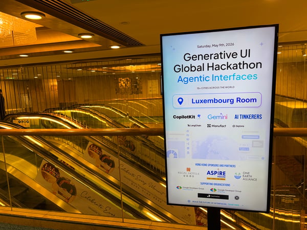 A digital display sign for the 'Generative UI Global Hackathon' stands in a hotel lobby area next to a set of escalators.