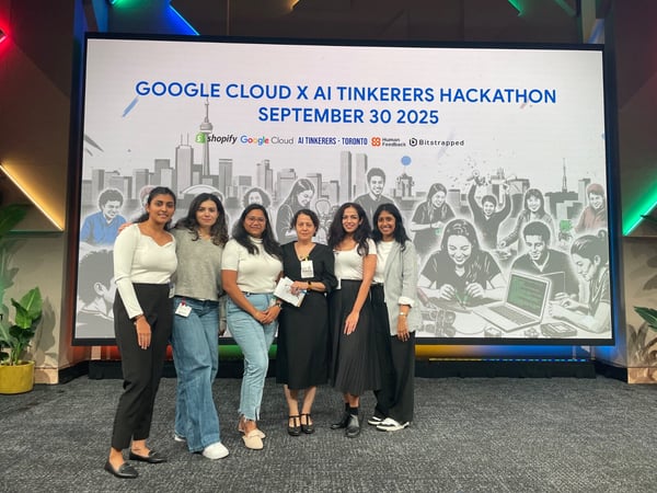 A photo shows six women posing together on a stage in front of a large screen displaying the branding and details for the 'Google Cloud X AI Tinkerers Hackathon'.