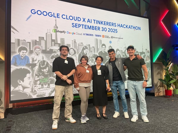 A group of five individuals stands together, posing for a photo in front of a large screen displaying the title of an event: 'GOOGLE CLOUD X AI TINKERERS HACKATHON SEPTEMBER 30 2025'.