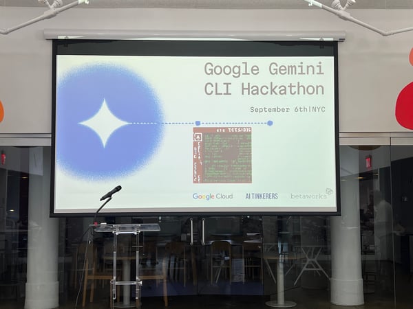 A photograph showing an indoor event setup featuring a large projection screen displaying the title slide for the 'Google Gemini CLI Hackathon'.