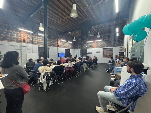 A group of people attending a presentation in an industrial-style indoor space with exposed brick walls and high ceilings.